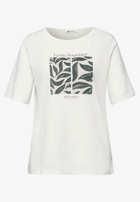 Wit T-shirt met korte mouwen, groen bladmotief in het midden en tekst 'La Vie Intemporelle' en 'Christine'.