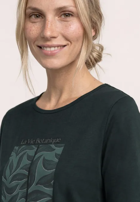 Eine Frau trägt ein schwarzes T-Shirt mit botanischem Muster und Schriftzug "La Vie Botanique".