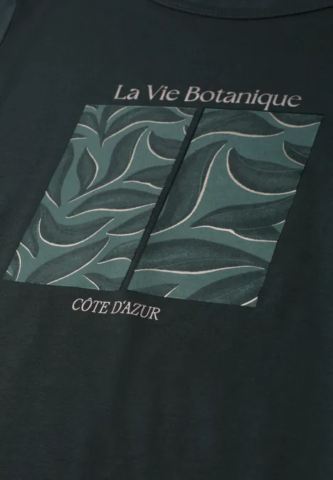 Schwarzes T-Shirt mit botanischem Print aus grünen Blättern und den Schriftzügen 'La Vie Botanique' und 'Côte d'Azur'.
