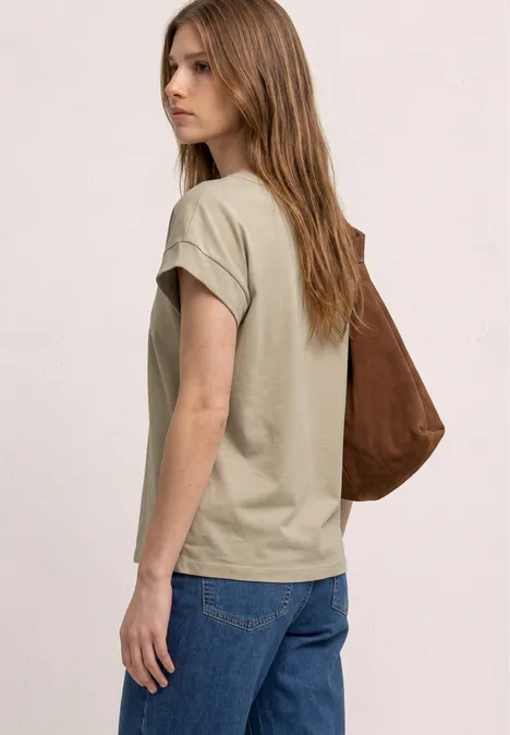 Frau in beiger T-Shirt und Jeans trägt braune Umhängetasche, seitliche Ansicht.