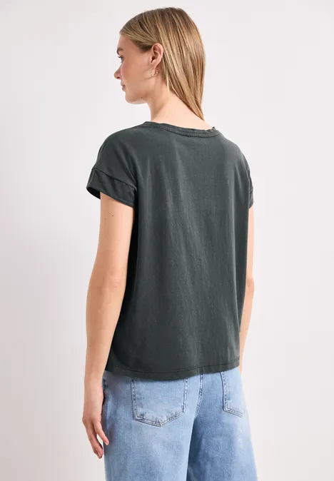 Eine Frau von hinten, trägt schwarzes T-Shirt und helle Jeans, steht vor hellem Hintergrund.