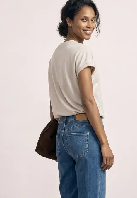Frau trägt weißes T-Shirt, blaue Jeans und Tasche, schaut über ihre Schulter.