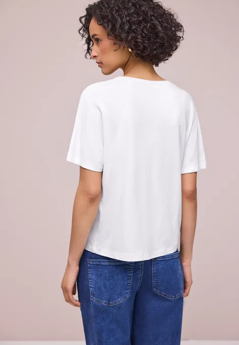 Eine Person von hinten in weißem T-Shirt und blauen Jeans.