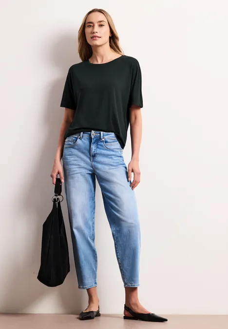 Frau trägt schwarzes T-Shirt, helle Jeans, schwarze Ballerinas und hält eine schwarze Tasche.