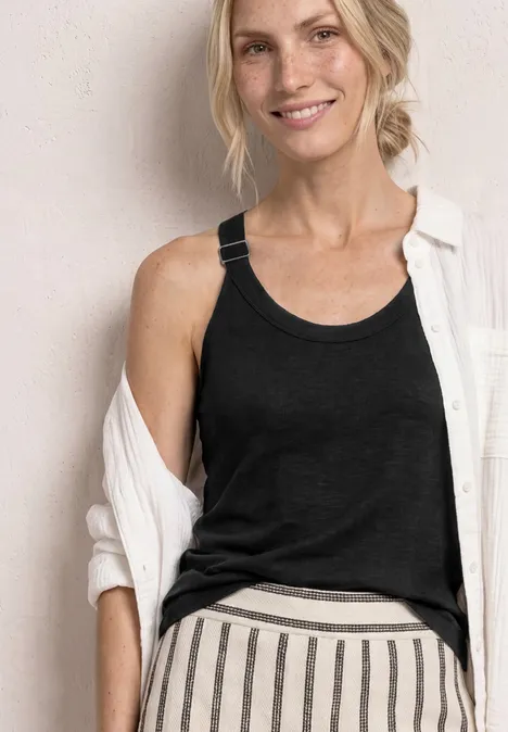 Frau mit verschwommenem Gesicht, schwarzem Tanktop, weißer Overshirt und gestreifter Hose.