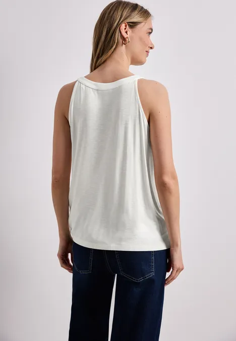 Rückansicht einer Frau in ärmellosem weißen Top und blauen Jeans vor hellem Hintergrund.