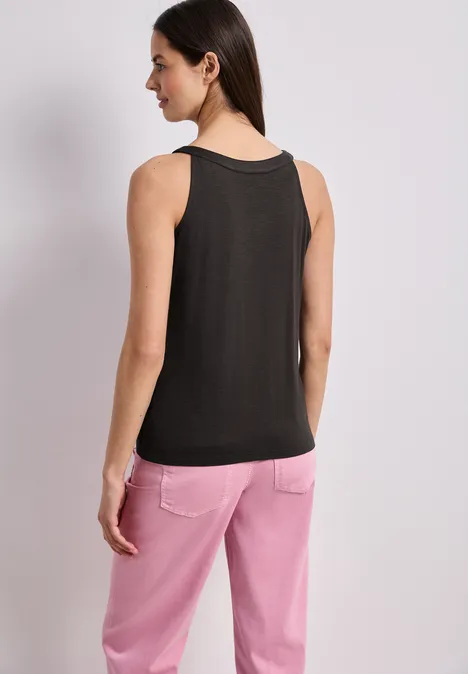 Frau, Rückenansicht, trägt schwarzes ärmelloses Top und rosa Hose vor hellem Hintergrund.