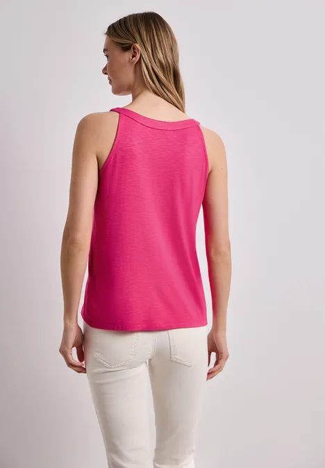 Frau von hinten in pinkem ärmellosem Top und heller Hose vor hellem Hintergrund.