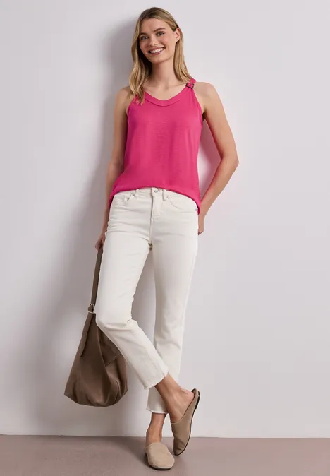 Frau in pinkem Tanktop, weißen Jeans und beigen Slippern mit passender Tasche vor neutralem Hintergrund.