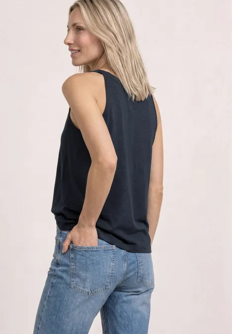 Een persoon van achteren in een mouwloos topje en jeans, handen in de achterzakken.