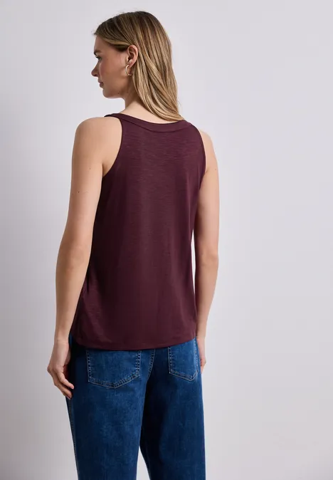 Frau von hinten in burgunderfarbenem Tanktop und blauen Jeans, mittellange blonde Haare.