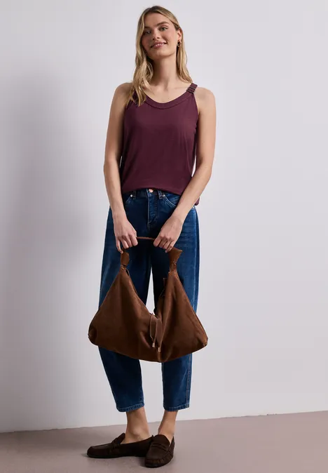 Frau in lockerer Jeans und ärmellosem Top hält eine braune Tasche.