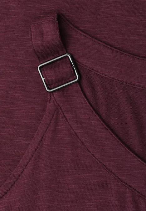 Nahaufnahme eines burgunderroten Kleidungsstücks mit verstellbarem Träger und quadratischem Metallverschluss.