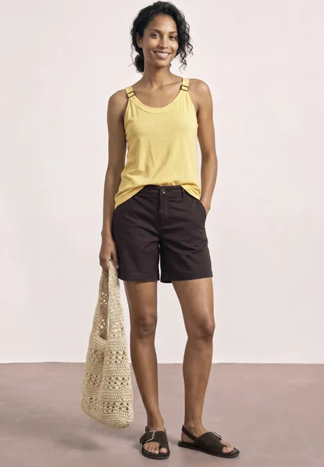 Vrouw draagt geel hemdje, donkere shorts, zwarte sandalen en houdt een netzak vast.