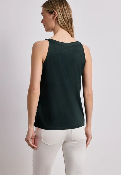 Frau von hinten in grünem Top und weißer Hose vor neutralem Hintergrund.