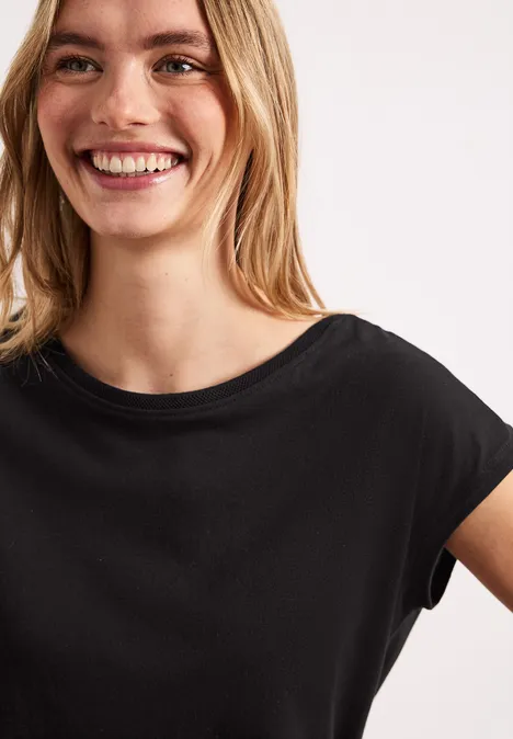 Eine Frau trägt ein schlichtes schwarzes T-Shirt mit überschnittenen Ärmeln.