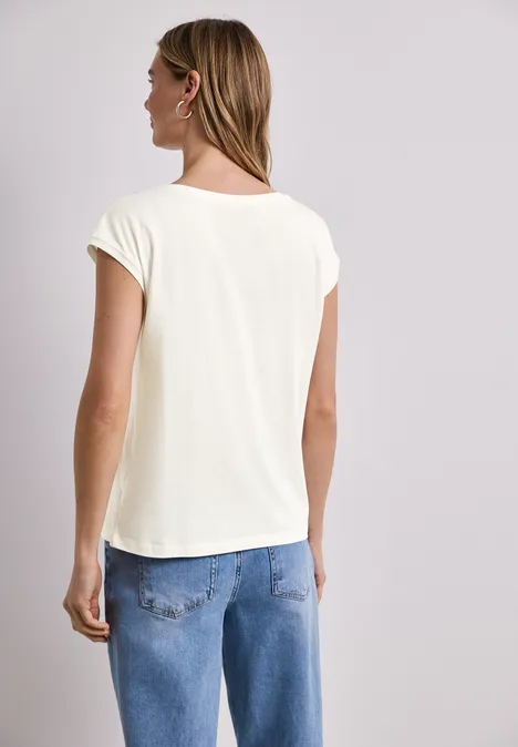 Frau mit blonden Haaren trägt weißes T-Shirt und blaue Jeans, Rückenansicht.