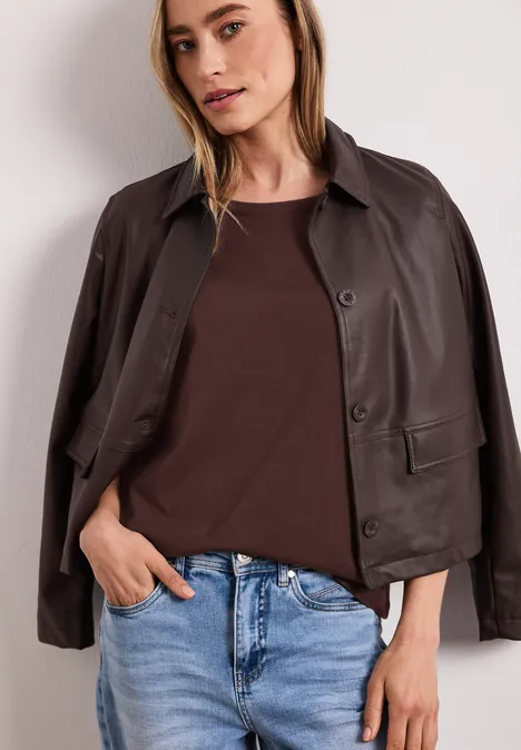 Frau trägt braune Lederjacke über dunkelbraunem Shirt und hellblaue Jeans.