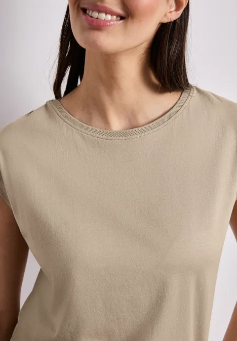 Een lachende vrouw draagt een mouwloze, beige top.