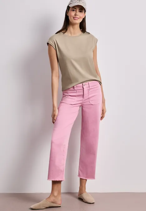 Vrouw draagt beige mouwloze top, roze recht gesneden jeans en beige loafers tegen lichte achtergrond.