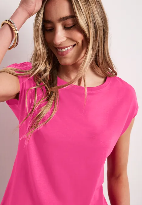 Vrouw in een felroze t-shirt, zijwaarts gekeerd, lange blonde haren en een armband om haar pols.