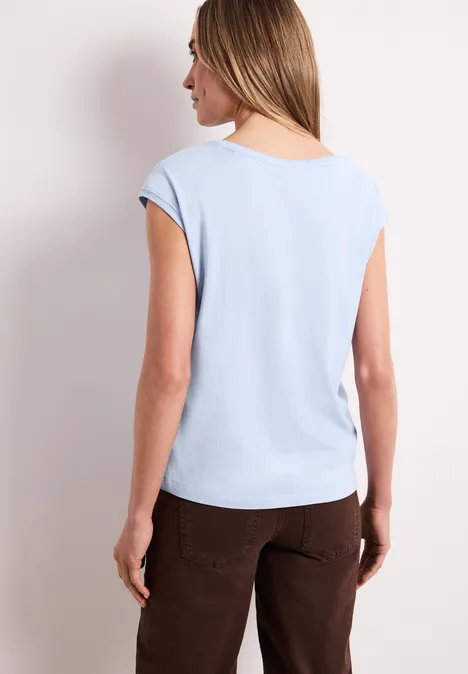 Frau steht von hinten, trägt hellblaues T-Shirt und braune Hose.