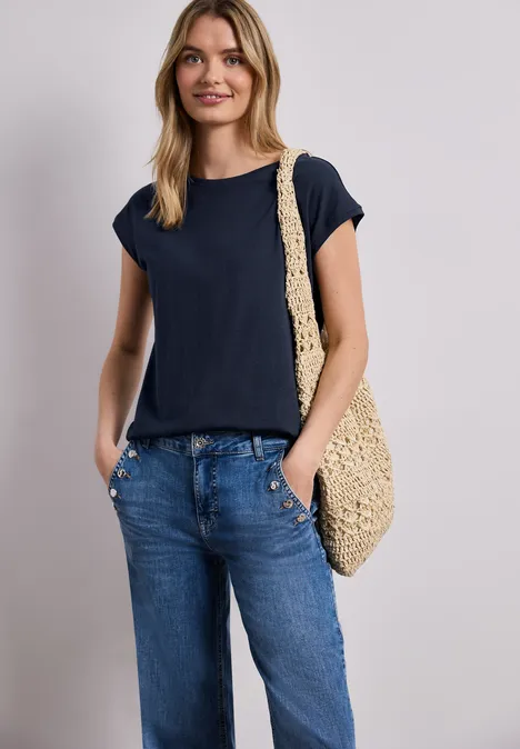 Frau in marineblauem T-Shirt und lockeren Jeans mit gehäkelter Umhängetasche.