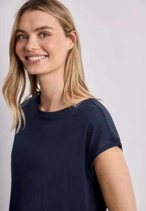 Eine Frau in T-Shirt vor hellem Hintergrund, Gesicht unkenntlich gemacht