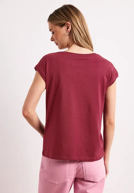 Vrouw van achteren in een bordeauxrood T-shirt en roze jeans voor witte achtergrond.