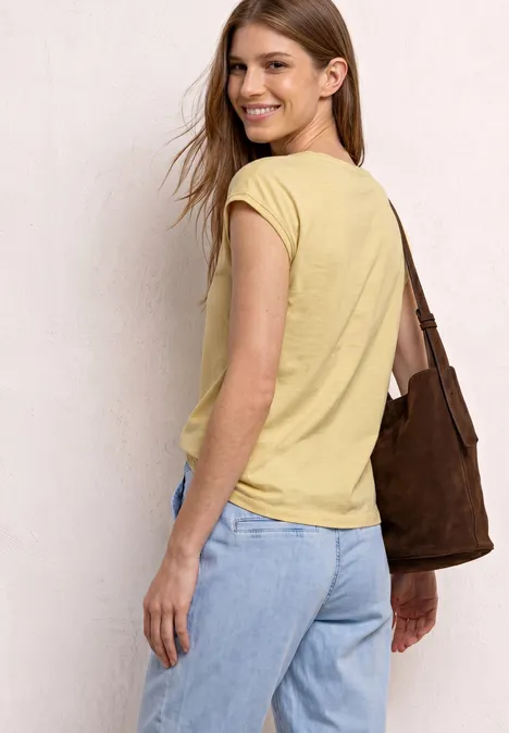 Eine Frau von hinten in gelbem T-Shirt und blauer Jeans mit brauner Schultertasche.