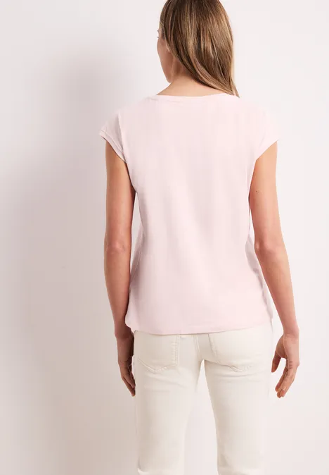 Vrouw van achteren in lichtroze t-shirt en crèmekleurige broek voor een lichte achtergrond.