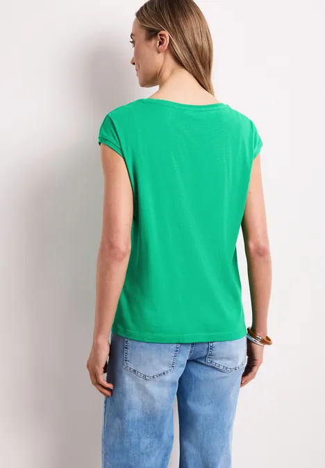 Een vrouw staat met haar rug naar de camera, draagt een groen T-shirt en blauwe jeans.