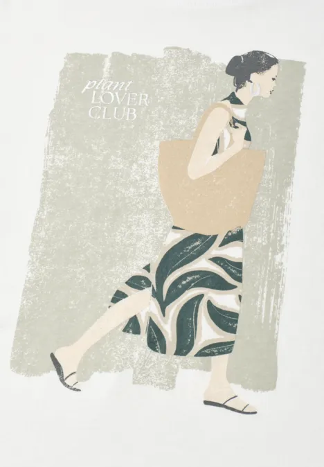 Vrouw in jurk met patroon en grote tas, lopend tegen een beige, getextureerde achtergrond.