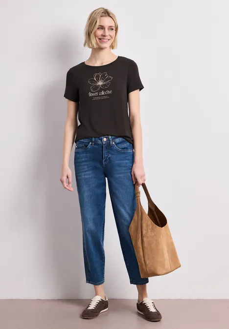 Schlichtes Outfit: Frau in schwarzem T-Shirt und blauen Jeans mit Einkaufstasche.