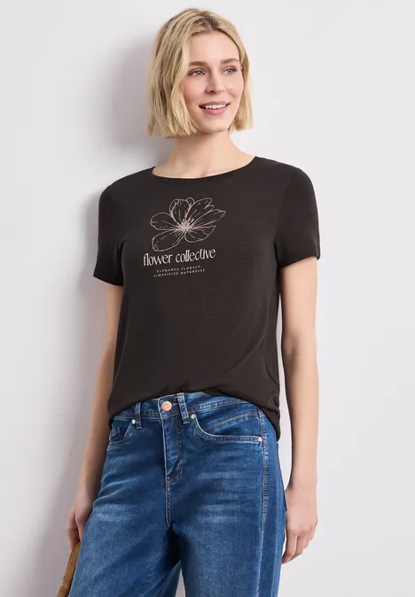 Frau trägt schwarzes T-Shirt mit ‚inner alchemie‘-Aufdruck und blauer Jeans.