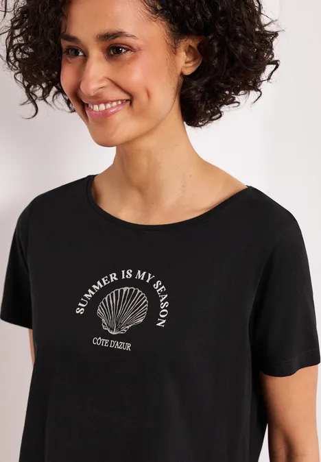 Person in schwarzem T-Shirt mit Muschelmotiv und der Aufschrift "SUMMER IS MY SEASON"