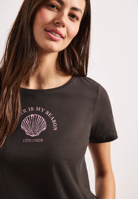 Nahaufnahme einer Frau im schwarzen T-Shirt mit Muschel-Logo und Schriftzug 'Sea is my season'.
