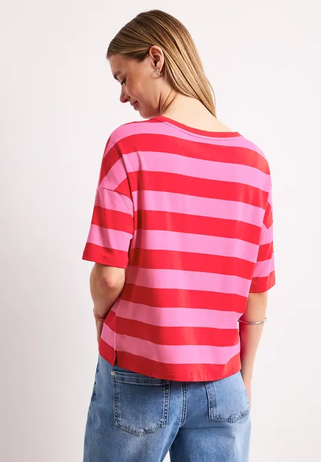 Vrouw van achteren met rood-roze gestreept t-shirt en blauwe jeans voor een witte achtergrond.
