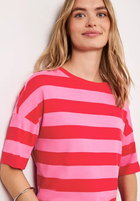 Jonge vrouw lacht, draagt roze-rood gestreept T-shirt met korte mouwen tegen lichte achtergrond.