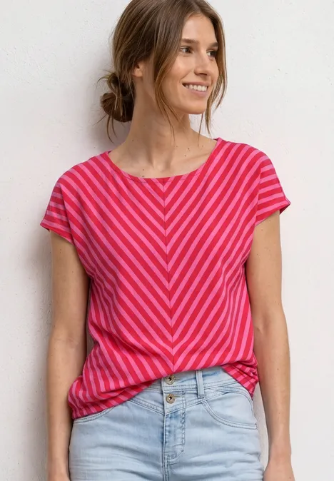 Frau trägt pink-rot gestreiftes T-Shirt und Jeans vor weißem Hintergrund.