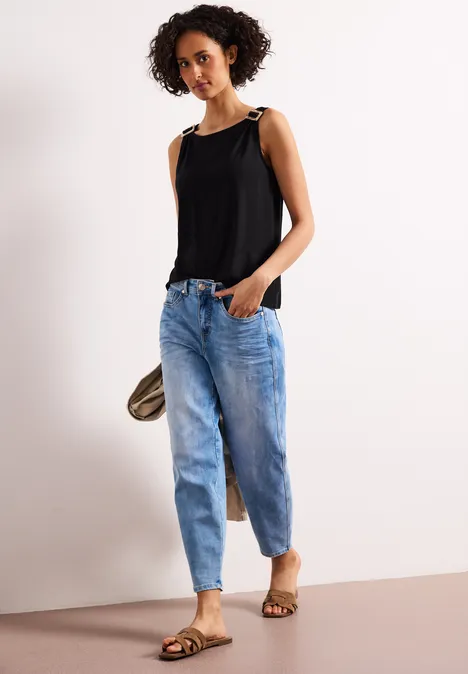 Frau in schwarzem ärmellosem Top mit Schulterbändern, blauen Jeans und Sandalen