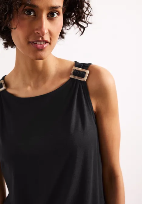 Nahaufnahme einer Person in ärmellosem schwarzen Oberteil mit silbernen Schnallen an den Trägern.