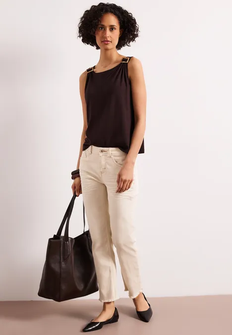 Persoon in zwarte mouwloze top, beige broek en zwarte ballerina’s, met een zwarte leren tas in de hand.