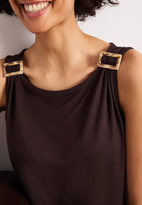 Close-up van glimlachende vrouw in bruin mouwloos topje met goudkleurige gespen op de schouderbanden.