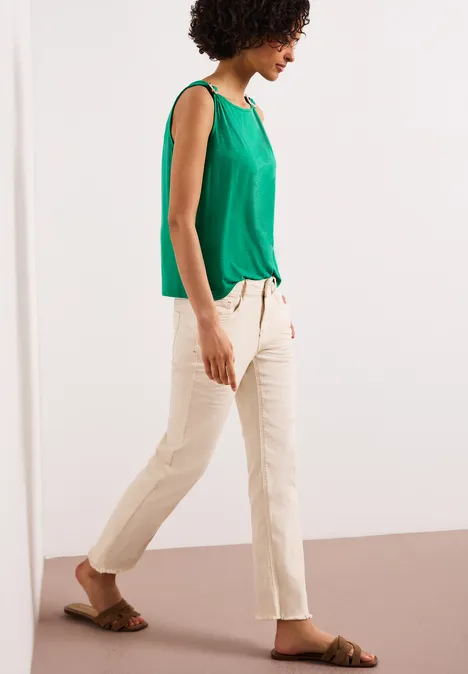 Seitlich gehende Frau in grüner Bluse, beiger Hose und Sandalen.