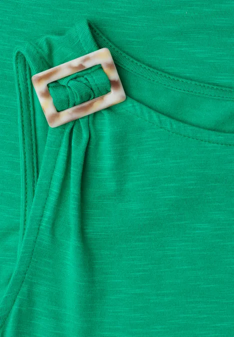 Grüner Stoffstreifen mit eckiger, heller Schnalle an der Schulter.