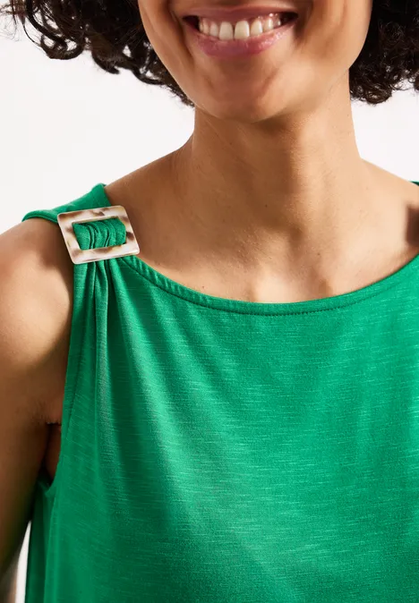 Eine Frau mit lockigem Haar trägt ein grünes Kleid mit einem Schulterriemen und einer Schnalle.