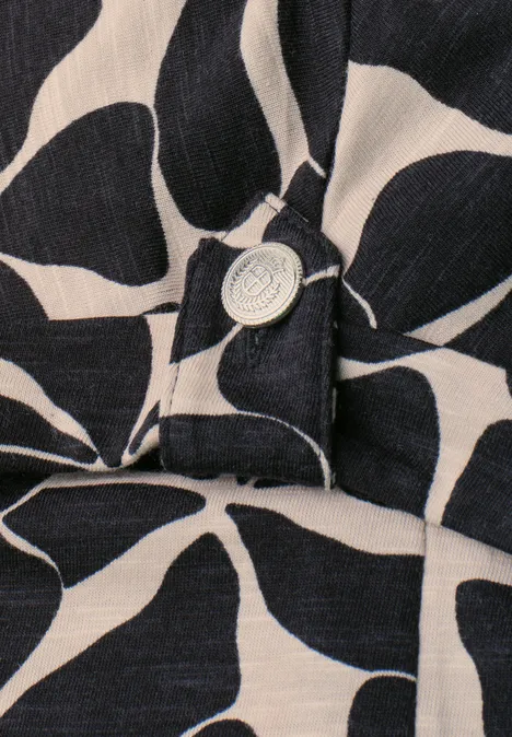 Close-up van donkerblauw-beige stof met groot bloemmotief en een zilverkleurige knoop.