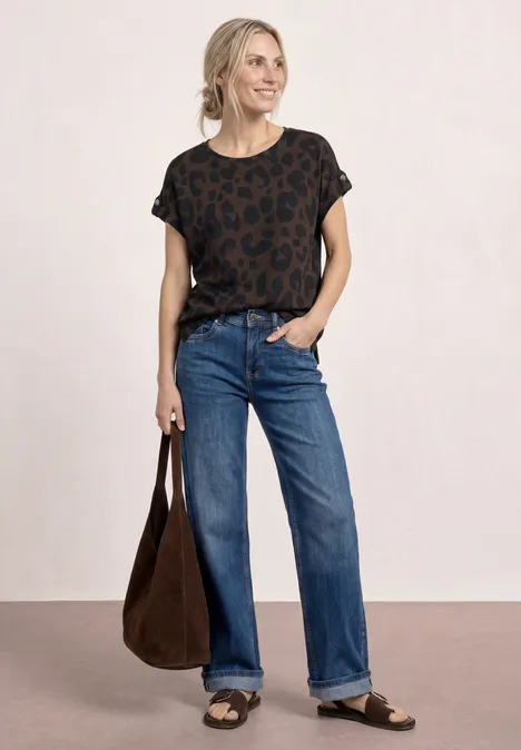 Frau in lässigem Outfit: gemustertes schwarzes Shirt, weite Jeans, Sandalen und große braune Tasche.