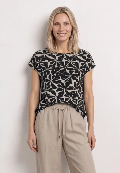 Frau im schwarzen T-Shirt mit großem weißen Blumenmuster und beigen, lockeren Hosen
